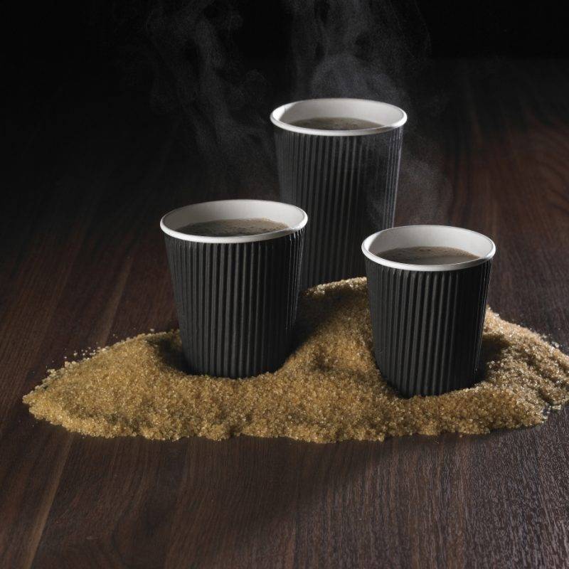 Hot drinks cups in black ripple design with pile of brown sugar