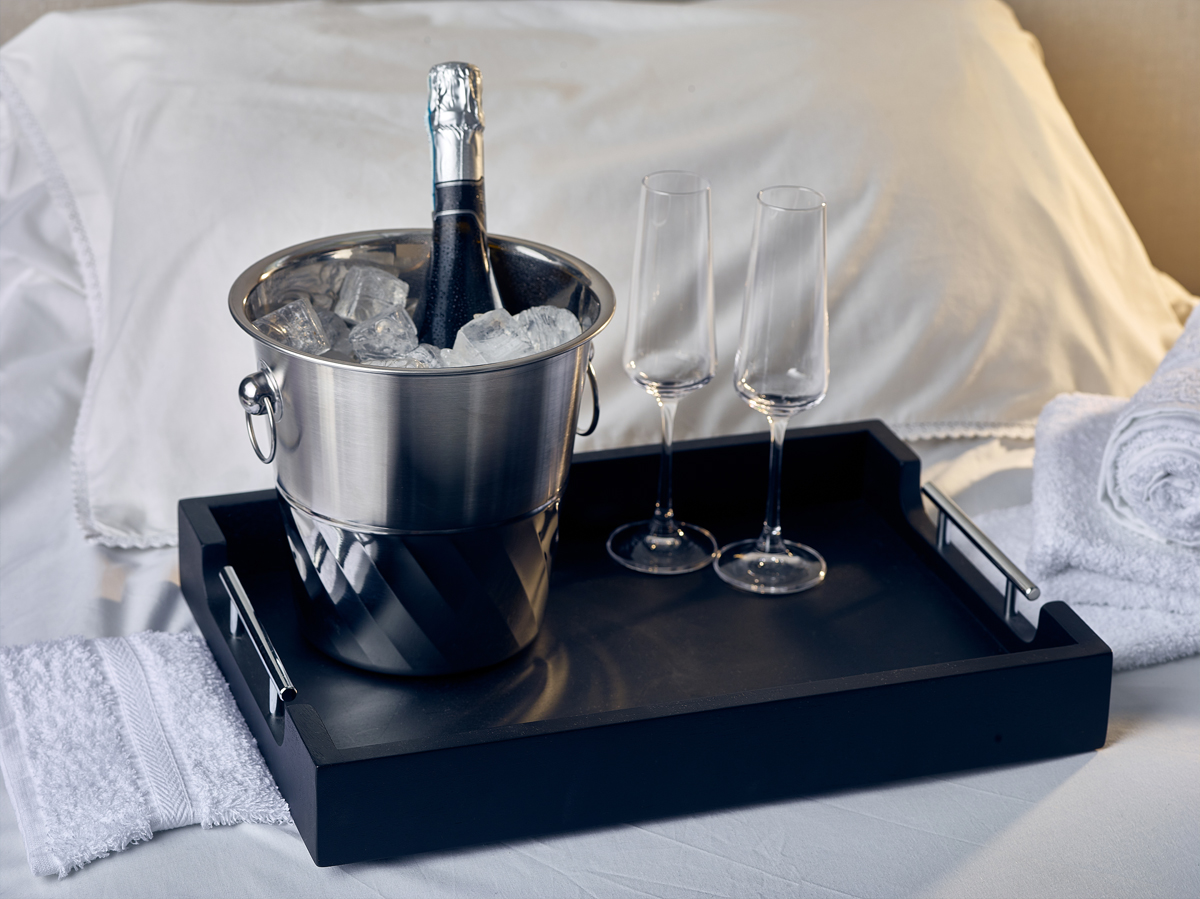 Black Butler Tray with champagne on ice, placed on a hotel bed.