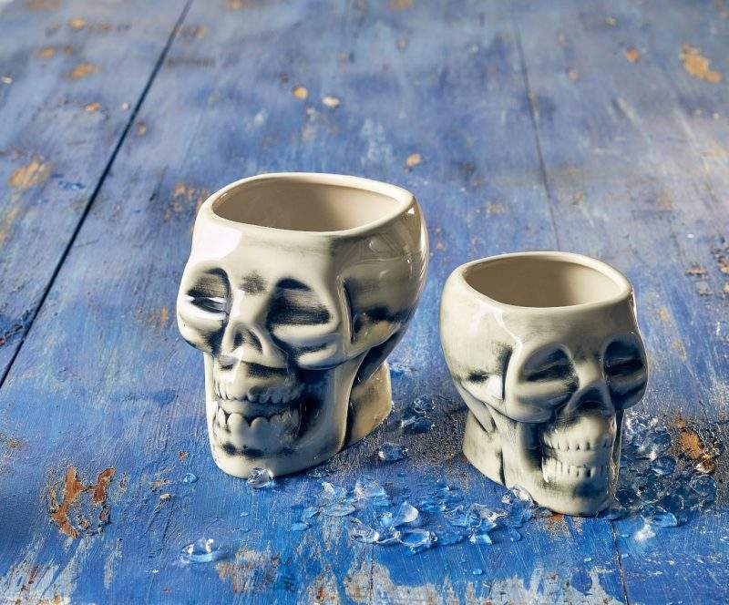Lifestyle image of two sizes of white skull tiki mugs